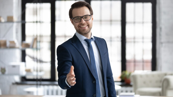 Happy,Young,Businessman,In,Glasses,Looking,At,Camera,,Reaching,Out