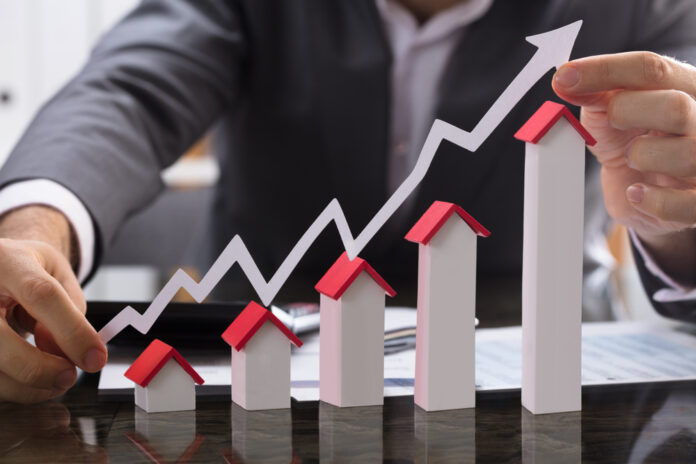 Businessman,Holding,Paper,Graph,Over,The,Increasing,House,Miniature